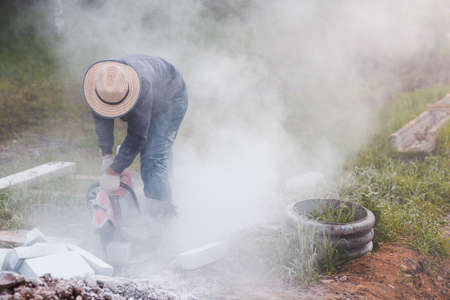 Worker mason cuts the sidewalk tile with circular saw while repairing sidewalk in city street.の写真素材