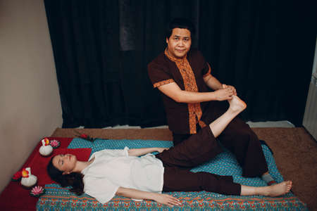 Thai man making classical thai massage procedure to young woman at beauty spa salonの写真素材