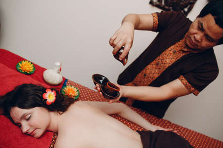 Thai man making classical thai massage procedure to young woman at beauty spa salonの写真素材