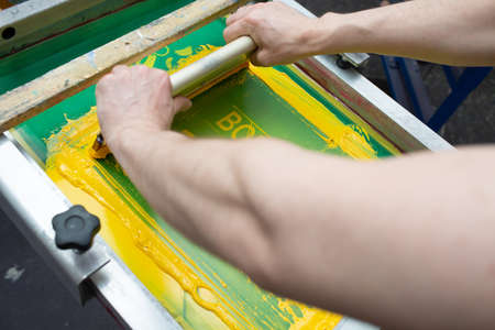 Serigraphy silk screen print process at clothes factory. Frame, squeegee and plastisol color paints.の写真素材
