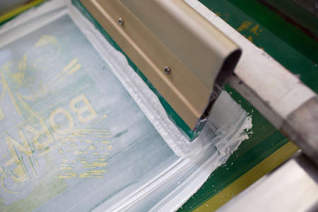 Serigraphy silk screen print process at clothes factory. Frame, squeegee and plastisol color paints.の写真素材