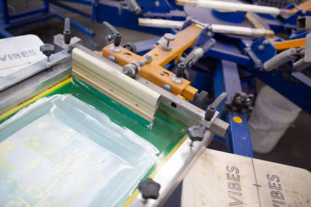 Serigraphy silk screen print process at clothes factory. Carousel Frame, squeegee and plastisol...