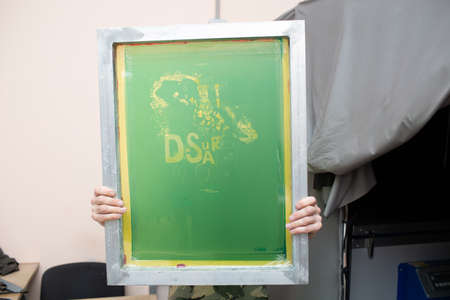 Serigraphy silk screen print process at clothes factory. Frame, squeegee and plastisol color paints.の写真素材