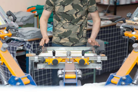 Worker printing picture application Serigraphy silk screen print process at clothes factory. Frame, squeegee and plastisol color paints.の写真素材