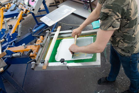 Serigraphy silk screen print process at clothes factory. Frame, squeegee and plastisol color paints.の写真素材