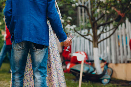 Man in jeans and a blue jacket stands with an empty wine glass in his hand.の写真素材