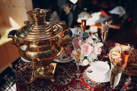 Old traditional Russian table for tea drinking with samovar, glasses of wine, flowers, pastries, bagels and bunsの写真素材