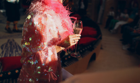 Woman in a pink dress with sequins holds a glass of champagne in her hand illuminated by the sun.の写真素材