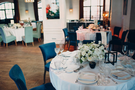 round tables in the restaurant with white tablecloths and white bouquets of flowers decor.の写真素材