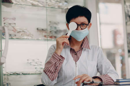 Portrait of an optometrist ophthalmologist middle aged adult woman wearing protective medical face mask.の写真素材