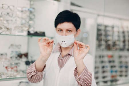 Happy Optician in Medical Face Mask Choosing Eyeglasses, female optometrist with glasses.の写真素材