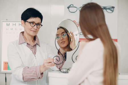 Young smiling woman smiling picking and choosing glasses at the optician corner at the shopping mall...
