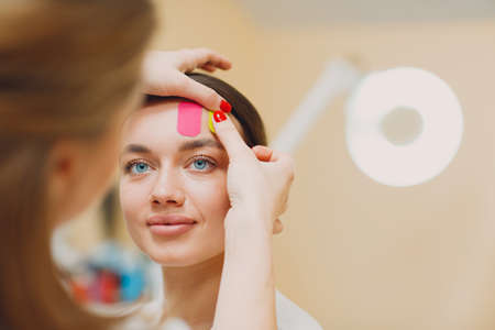 Beautiful woman applying tape lifting treatment procedure on faceの写真素材