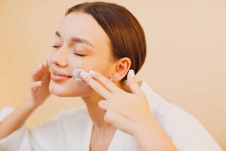 Young woman applying cosmetic white cream on faceの写真素材