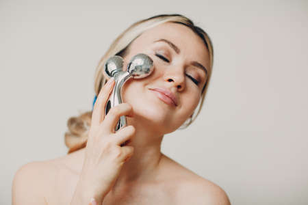 Beautiful young adult woman with massage face roller on beige backgroundの写真素材
