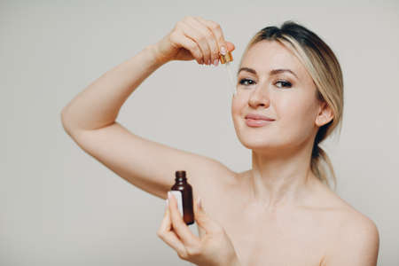 Cosmetic oil bottle hold applying with pipette on face of young womanの写真素材