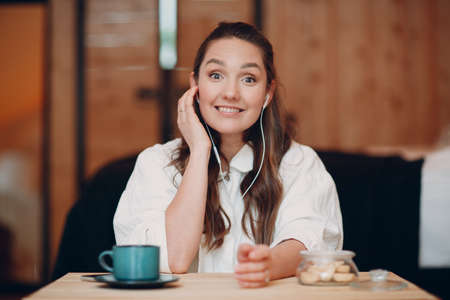 Smiling happy young woman sitting at table at home behind computer laptop and talking on video call. Girl female with portable mobile headphones speaking online on webcam indoorsの写真素材