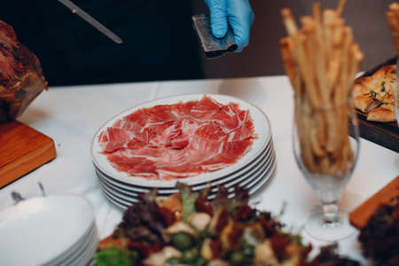 the waiter cuts the hamon with a knife and holds a piece of ham in the clamp in his hand.の写真素材