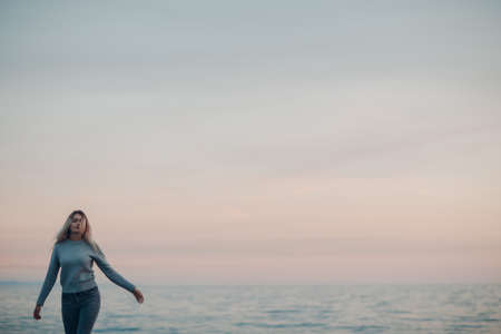 Young woman dressed in jeans and sweater on the seashore pebble beachの写真素材
