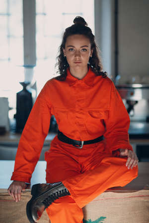 Young brunette curly woman in orange suit. Female in colorful overalls portraitの写真素材