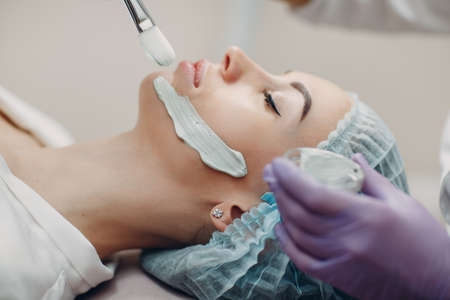 Young woman applying mask of clay on face in beauty spa.の写真素材