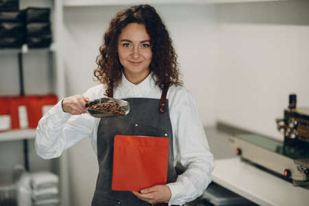 Fresh roasted coffee beans young worker woman packing machine in vacuum sealed bag.の写真素材