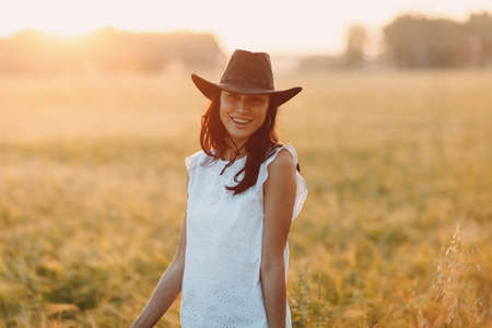 Woman farmer in cowboy hat at agricultural field on sunset.の写真素材