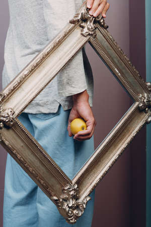 Millenial young man holds apple on hand palm in gilded picture frameの写真素材