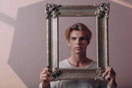 Millenial young man artist with blonde hair on gilded picture frame portrait.の写真素材