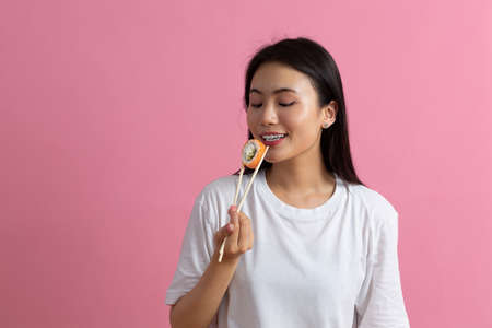 Asian beauty model girl going to eat Sushi roll, healthy japanese food. Beautiful woman holding chopsticks with Philadelfia roll.の写真素材
