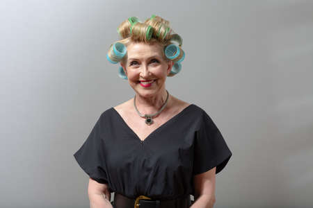 Elderly old aged woman smiling housewife with curlers rollers on hair head.の写真素材