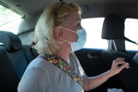 Elderly caucasian old aged woman take taxi car vehicle ride with face maskの写真素材