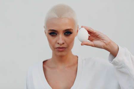 Portrait of young smiling millenial european short haired woman hold egg in hand. Beautiful happy...