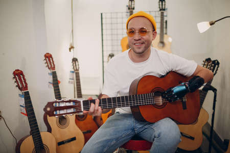 Young disabled man with artificial prosthetic hand plays on guitar at shopの写真素材