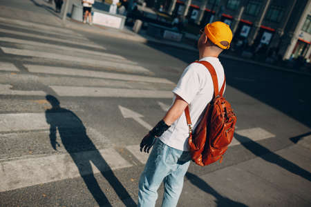 Young traveler disabled man with artificial prosthetic hand in casual clothes and backpack walking at sunny city street outdoor crosswalk arrows wayの写真素材