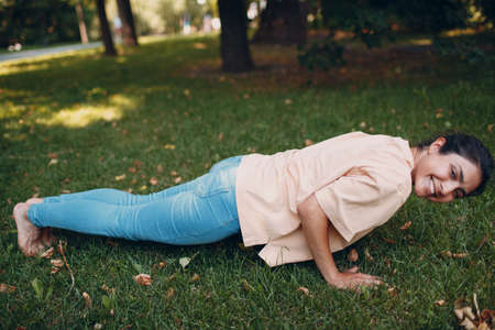 Adult young fitness indian woman doing push up and plank bar on grass in summer parkの写真素材