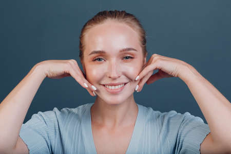 Millenial young woman blonde hair portrait doing face yoga self facebuilding massage for face skin.の写真素材