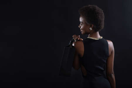 African american woman back view with afro hairstyle holds black shopping bags. Sale and discounts on market and Black Friday concept.の写真素材