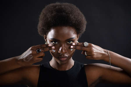 Beautiful young ethnic african american black woman applying moisturizer white cream on her face like american football playerの写真素材