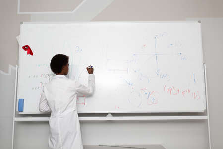 African American woman math teacher writing on blackboard with marker.の写真素材
