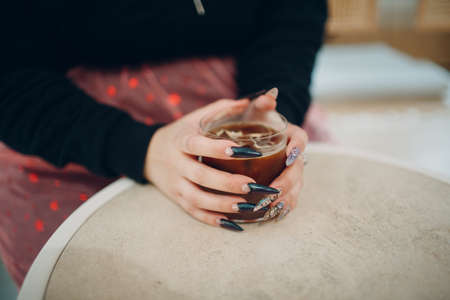 Female hands with manicure nails hold glass of coffee sitting in cafe with cupの写真素材