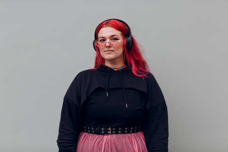 European plus size woman in headphones. Young red pink haired body positive girl.の写真素材