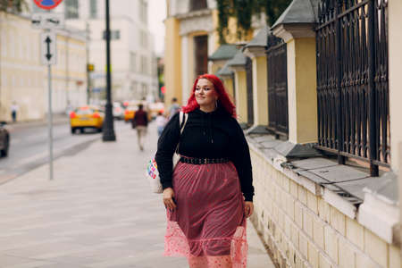 Young plus size woman. Young red pink haired body positive girl walking at city street outdoorsの写真素材