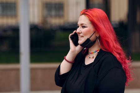 European plus size woman walking outdoor street city with mobile cellular phone. Young red pink haired body positive girl using cellphone smartphoneの写真素材