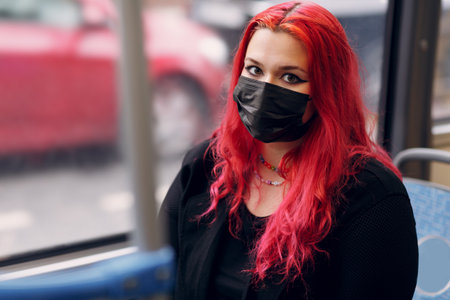 European plus size woman face mask riding bus transport. Young red pink haired body positive girl with facemaskの写真素材