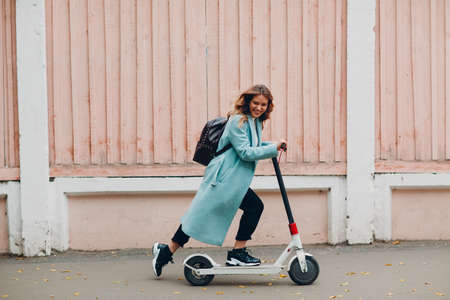 Young woman in coat ride electric scooter at the city in autumn weatherの写真素材