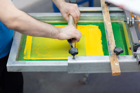 Serigraphy silk screen print process at clothes factory. Frame, squeegee and plastisol color paints.の写真素材