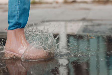 Woman wearing rain rubber boots walking running and jumping into puddle with water splash and drops in autumn rain.の写真素材