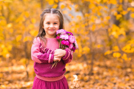 Cute little girl in fall park with pink flower bouquet.の写真素材