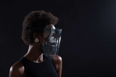 African american woman profile in black medical face mask and transparent protective face shield.の写真素材